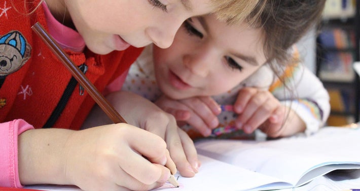 two young kids focusing on writing in a book
