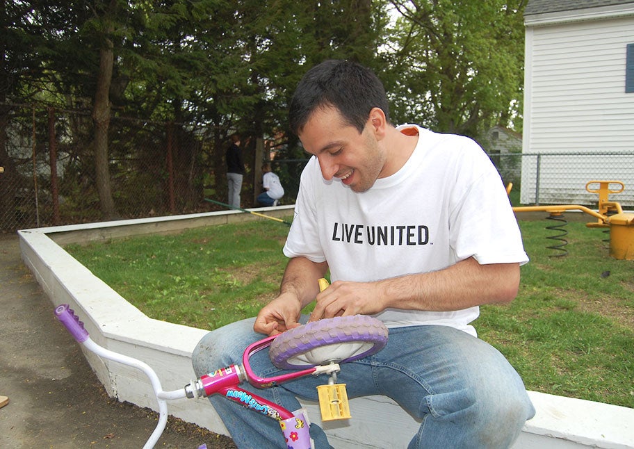 Unitil employee as United Way volunteer fixing kid's bike