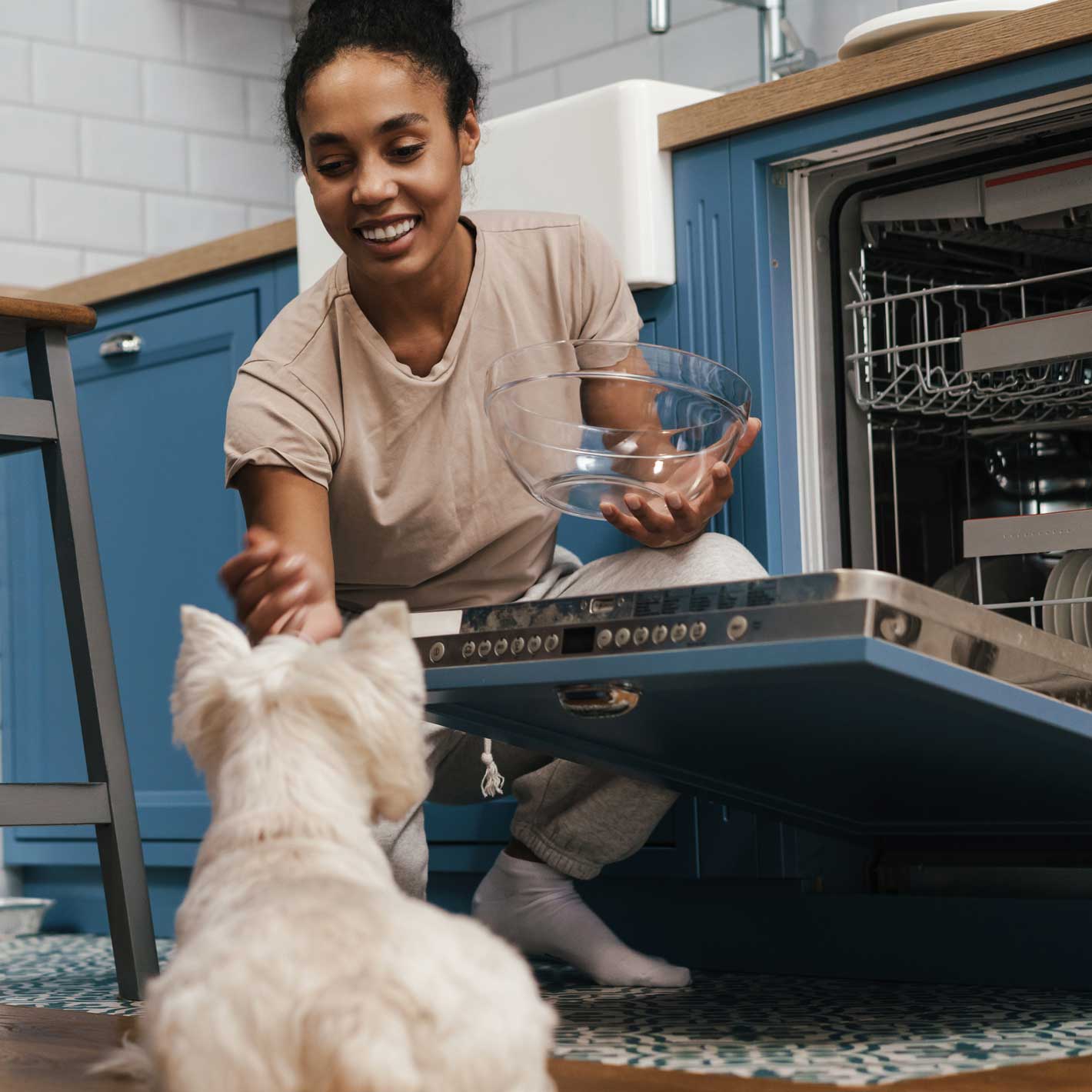 Young woman playing with her dog while emptying the dishwasher.