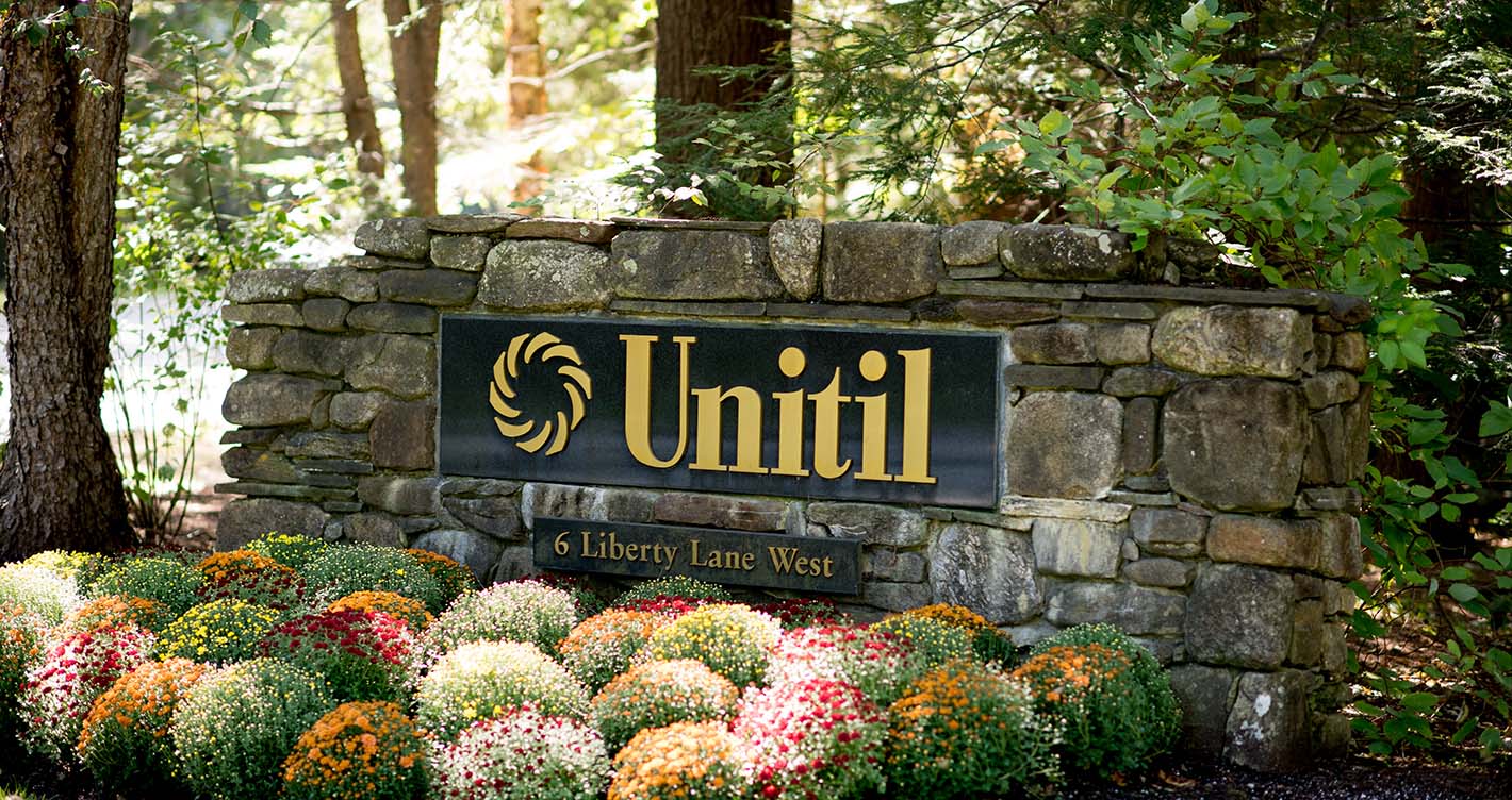 Unitil exterior office sign on a stone wall sitting behind a flower garden