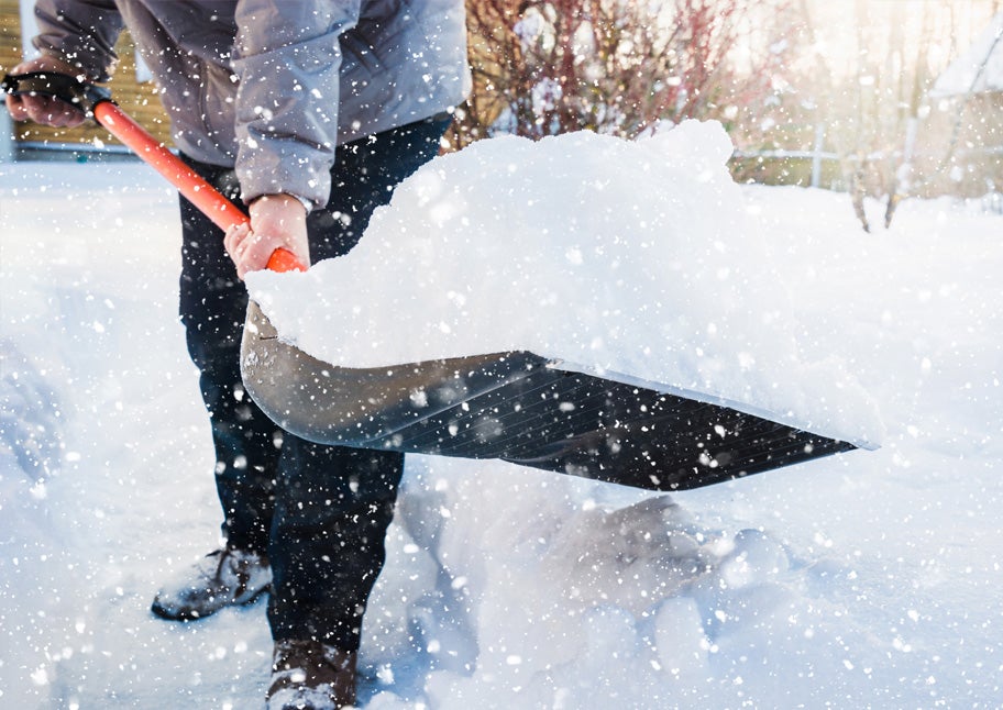 person with black pants holding orange handle snow shovel full of snow