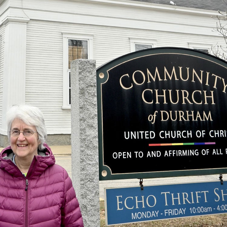 Unitil customer poses next to sign in front of white church.