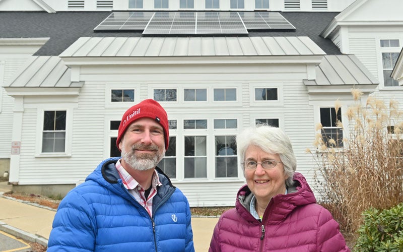 Unitil representative and customer pose in front of white church with solar panels.