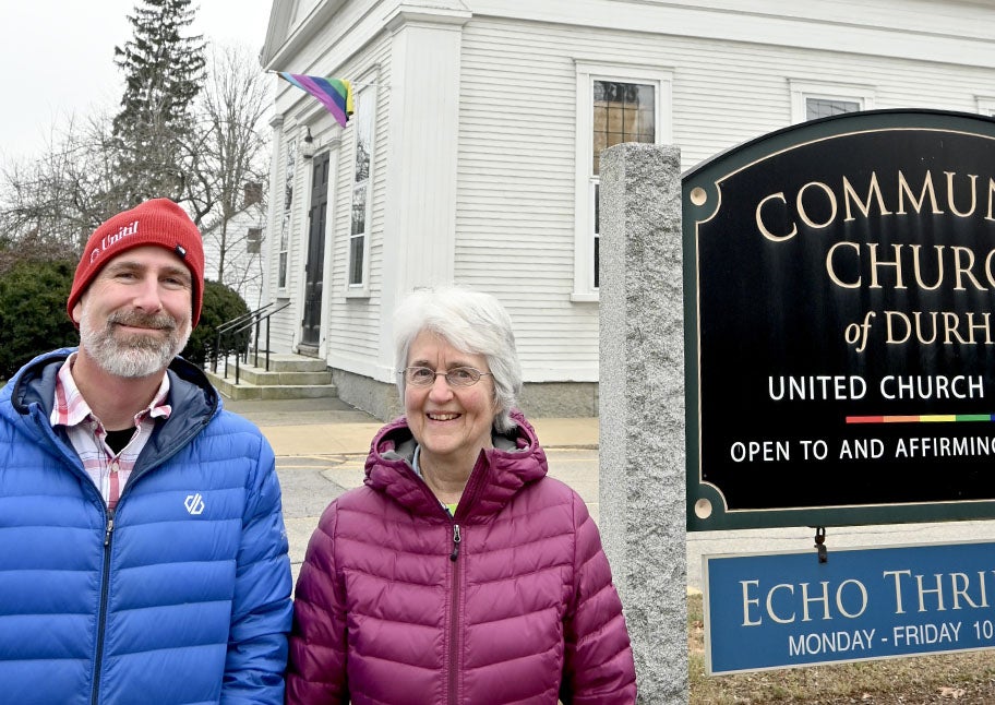 Unitil representative and customer pose next to sign in front of white church.