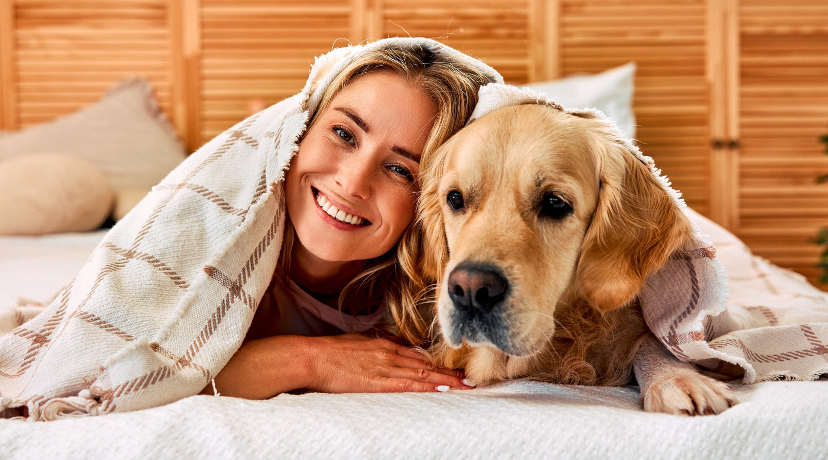 happy woman cuddles with dog under cozy blanket in home