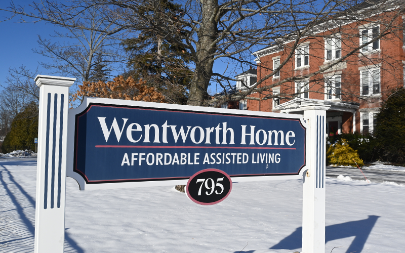 Sign of Wentworth Home in Dover, NH in front of the building with blue skies and snow on the ground