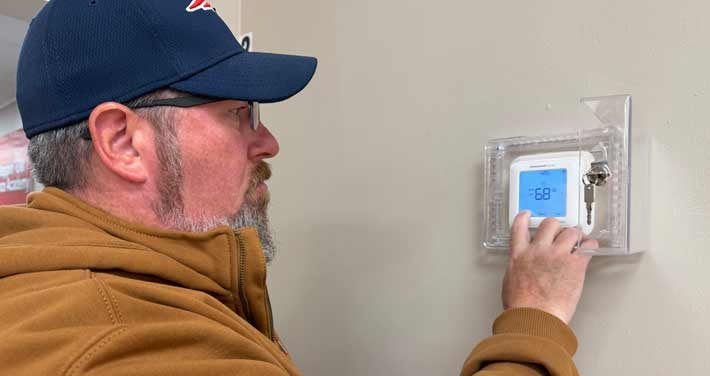 person with hand on wall thermostat set to 68 degrees