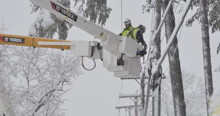 Unitil linemen in bucket truck next to snow covered wires