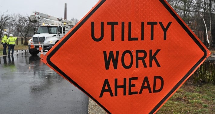 Utility work ahead sign with workers in the background