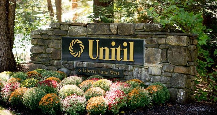 Unitil sign on stone wall with flower garden