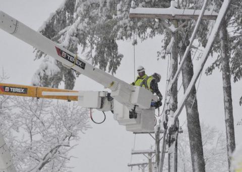 Unitil linemen in bucket truck next to snow covered wires
