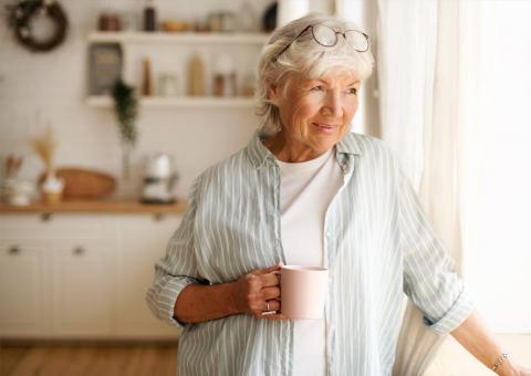 older lady stands with coffee in bright apartment