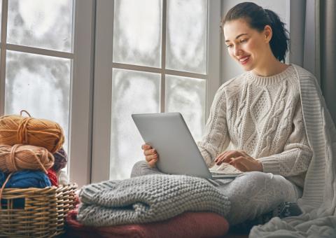 woman sitting in front of window with laptop and blankets