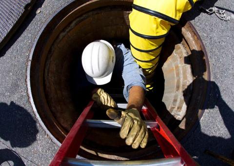 utility worker climbing down hole in street to repair underground wires