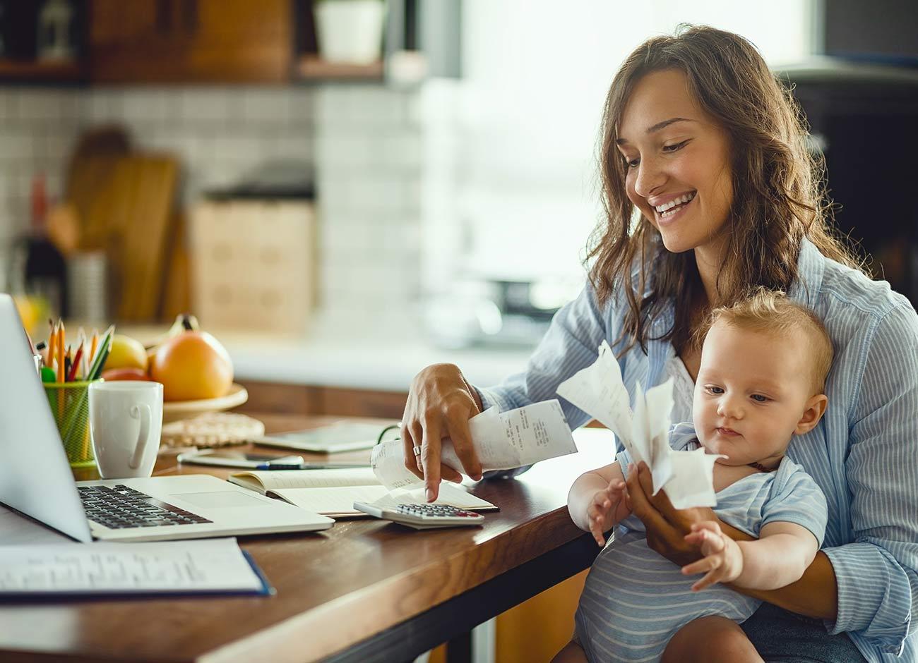 woman with baby paying bills at kitchen table